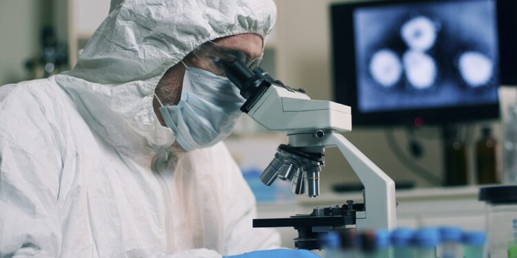 A research scientist working in his laboratory with a sample or specimen and an image of the Wuhan Coronavirus displayed on a computer screen.